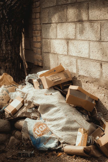 Two large black plastic garbage bags filled with waste materials are positioned on a paved sidewalk curb in an outdoor setting. The bags appear to be tightly knotted and are placed close to each other